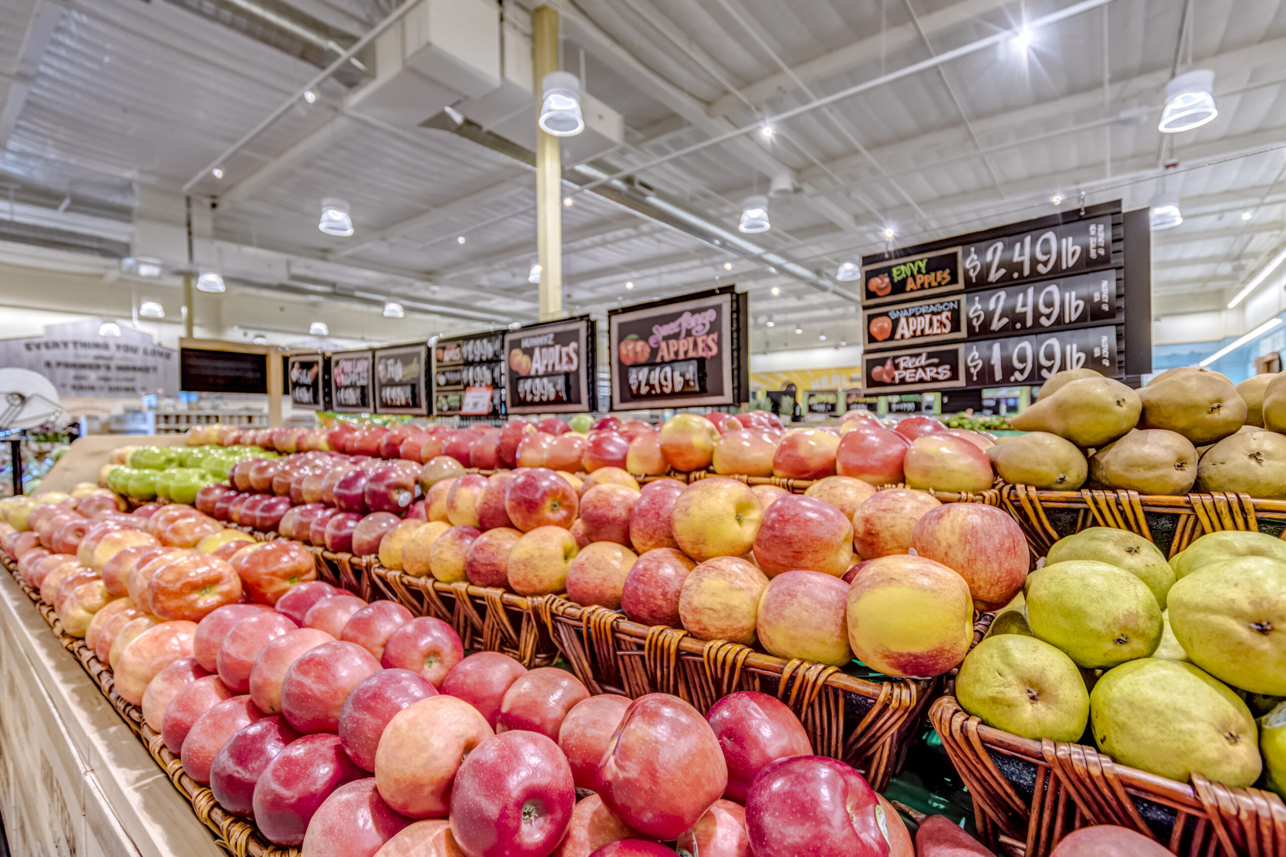 A wide selection of apples and pears in a brightly lit aisle of Sprout Farmers Market.